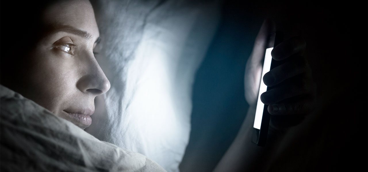Frau schaut nachts in ihrem Bett aufs Handy.