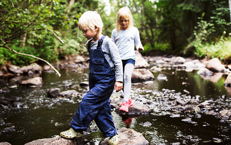 Junge und Mädchen spazieren über Steine im Flussbett.