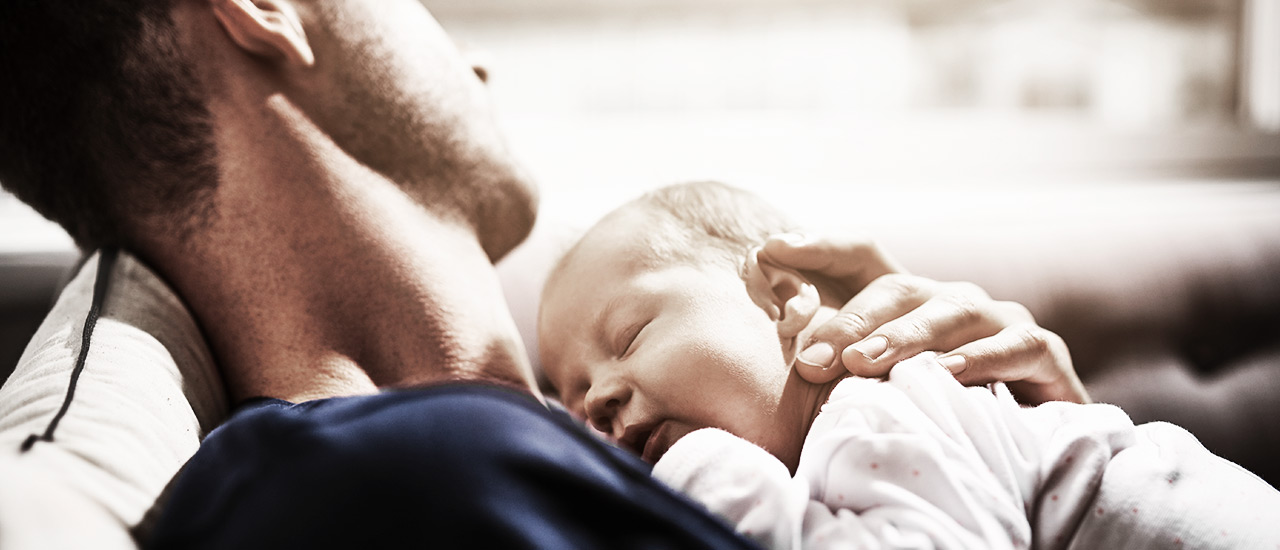 Mann hält schlafendes Baby im Arm.