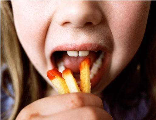 Kind steckt sich Pommes mit Ketchup in den Mund.