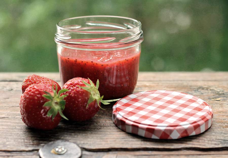 Ein Glas Erdbeer-Chia-Marmelade mit frischen Erdbeeren auf einem Tisch