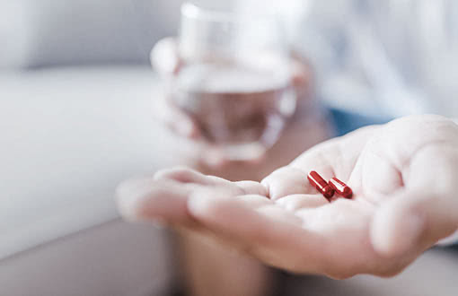 Zwei Tabletten in einer Handfläche und ein Glas Wasser im Hintergrund
