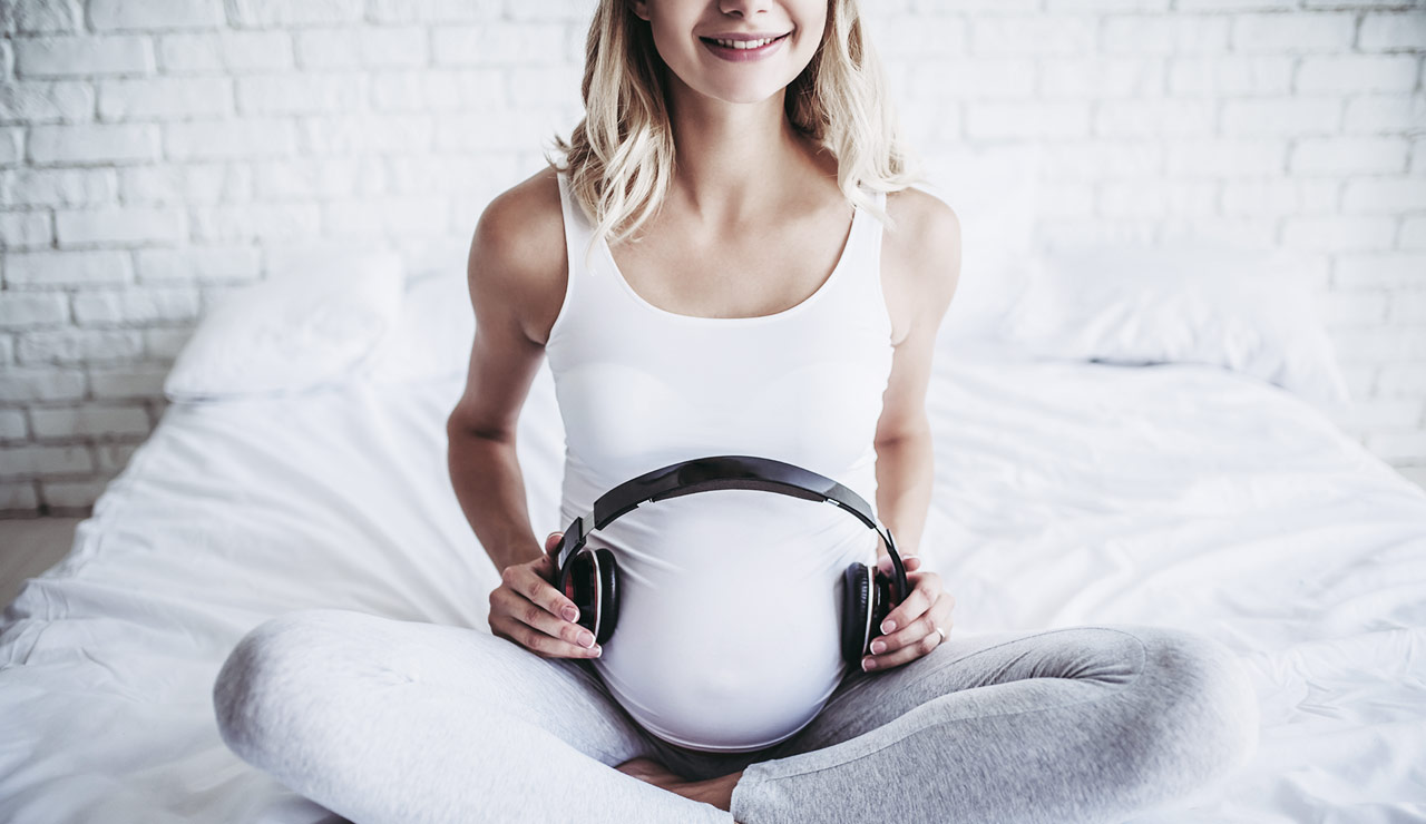 Schwangere hält Kopfhörer an Babybauch.